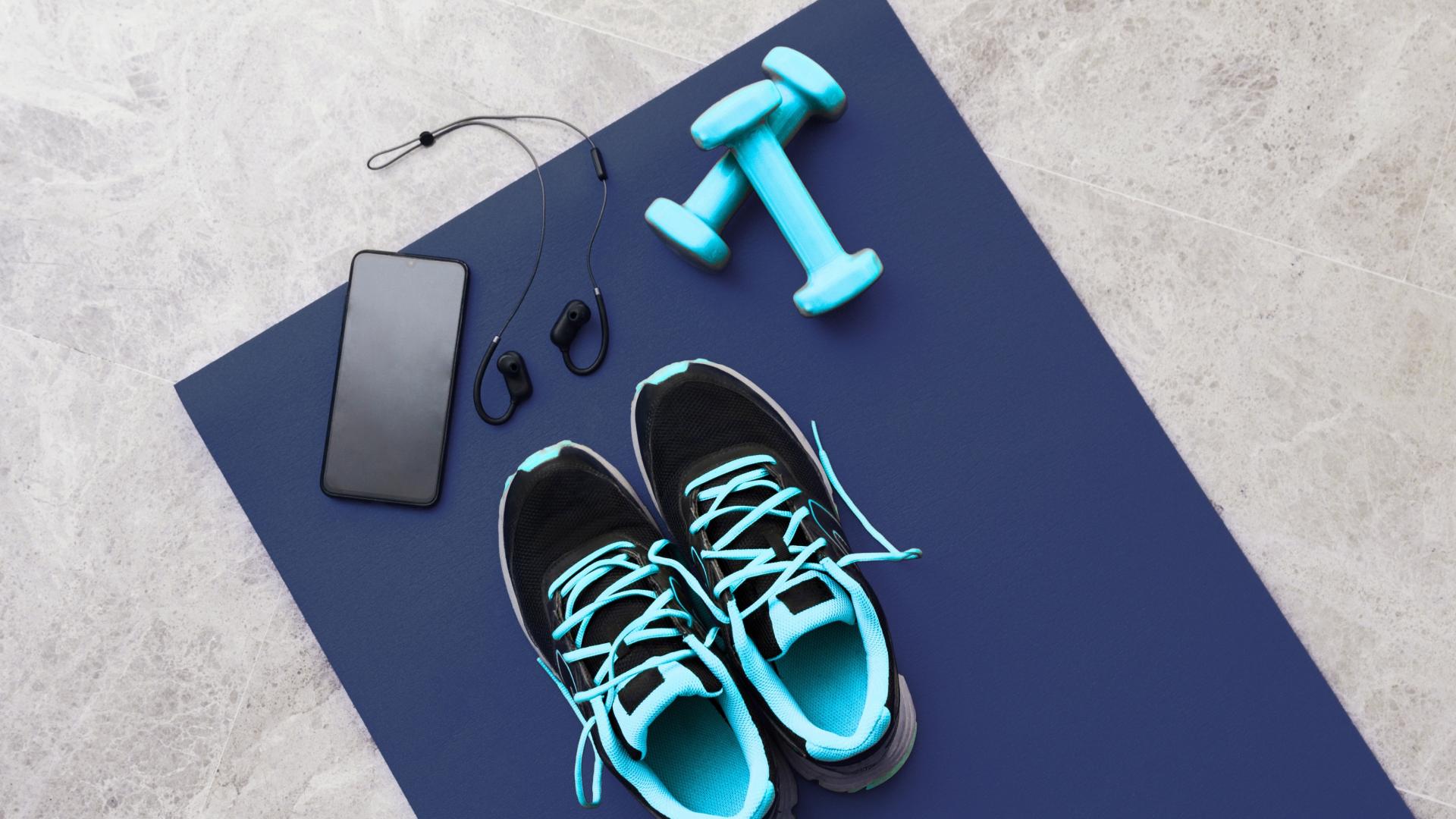 A yoga mat with weights, running shoes and a phone with earbuds