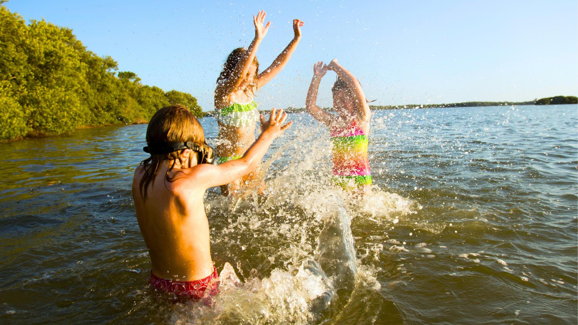 Three kids splashing each other in a lake