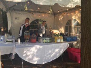 Catering table with a spread of food and drinks on it. There are two caterers tending to the table.