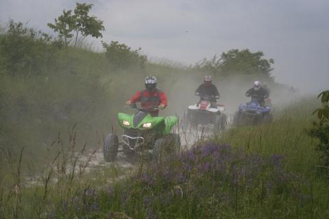 Group of three people riding ATVs through a dirt trail.